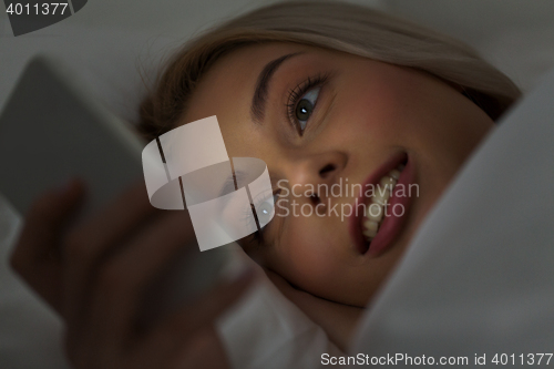 Image of young woman with smartphone in bed at night