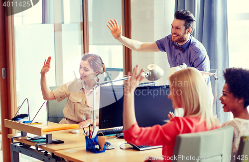Image of happy creative team waving hands in office