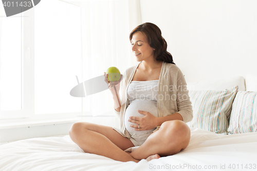 Image of happy pregnant woman eating green apple at home