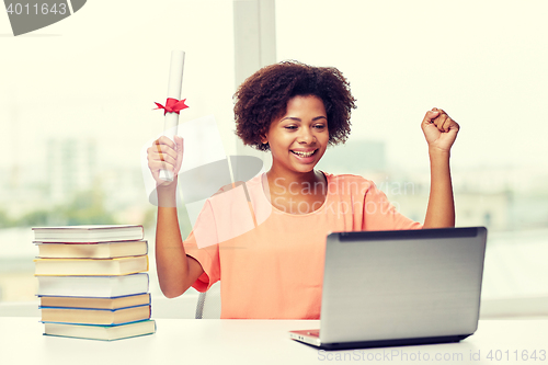 Image of happy african woman with laptop, books and diploma