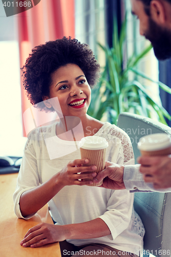 Image of happy woman taking coffee from man in office