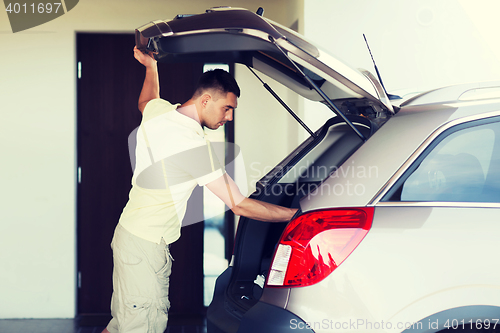 Image of young man with open car trunk at parking space