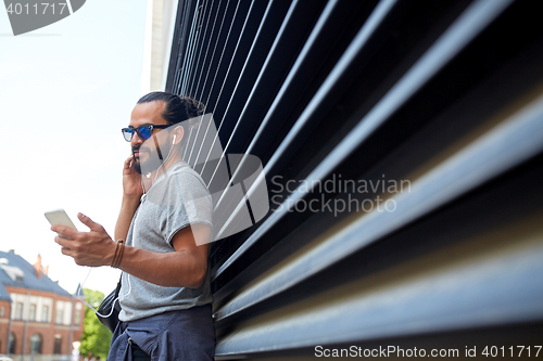 Image of man with earphones and smartphone on city street