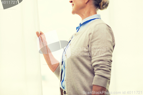 Image of happy senior woman looking through window at home