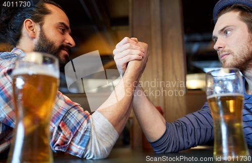 Image of male friends arm wrestling at bar or pub