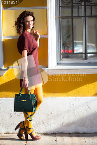 Image of beautiful smiling woman in a burgundy dress with green handbag