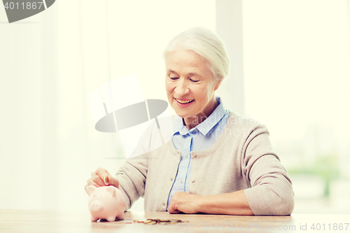 Image of senior woman putting money to piggy bank at home