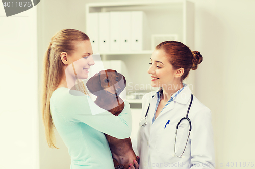 Image of happy woman with dog and doctor at vet clinic