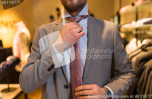 Image of close up of man tying tie at clothing store mirror