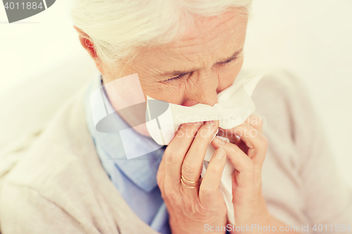 Image of sick senior woman blowing nose to paper napkin