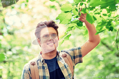 Image of smiling young man with backpack hiking in woods