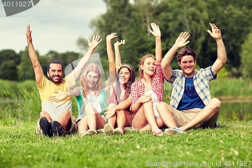 Image of group of smiling friends waving hands outdoors