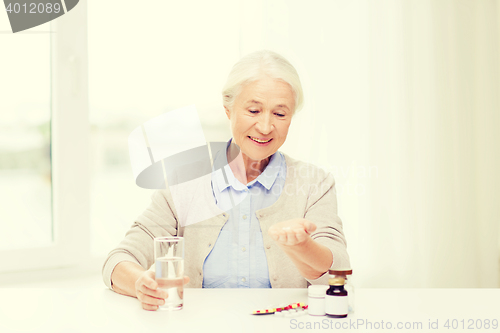 Image of happy senior woman with water and medicine at home