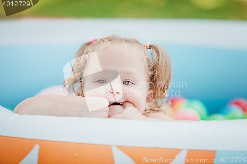 Image of The little baby girl playing with toys in inflatable pool in the summer sunny day