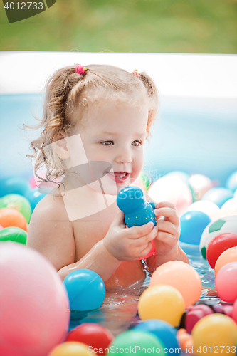 Image of The little baby girl playing with toys in inflatable pool in the summer sunny day