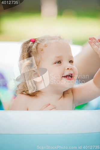 Image of The little baby girl playing with toys in inflatable pool in the summer sunny day
