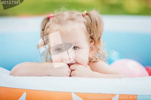 Image of The little baby girl playing with toys in inflatable pool in the summer sunny day