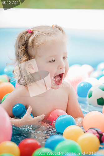 Image of The little baby girl playing with toys in inflatable pool in the summer sunny day