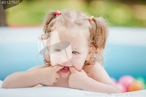 Image of The little baby girl playing with toys in inflatable pool in the summer sunny day