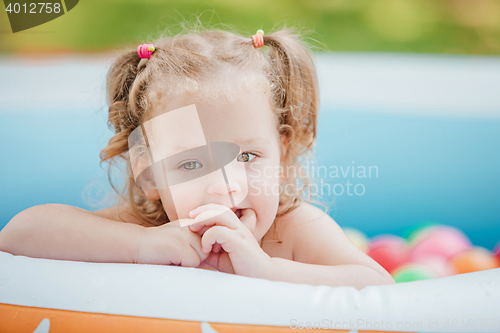 Image of The little baby girl playing with toys in inflatable pool in the summer sunny day