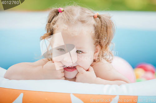 Image of The little baby girl playing with toys in inflatable pool in the summer sunny day