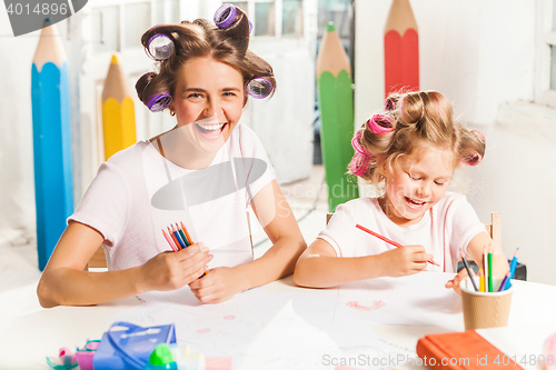 Image of The young mother and her little daughter drawing with pencils at home