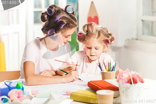 Image of The young mother and her little daughter drawing with pencils at home