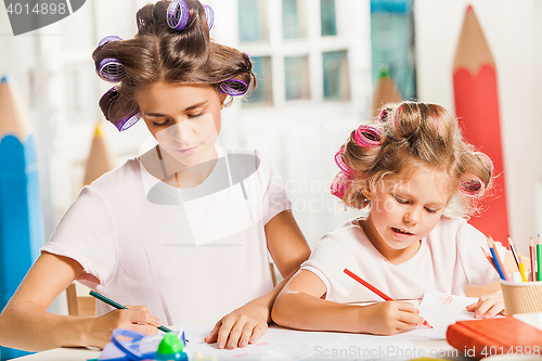 Image of The young mother and her little daughter drawing with pencils at home