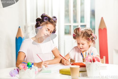 Image of The young mother and her little daughter drawing with pencils at home