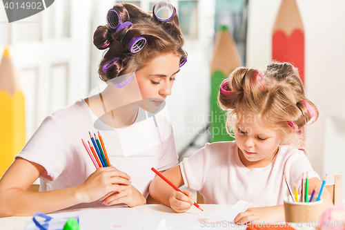 Image of The young mother and her little daughter drawing with pencils at home