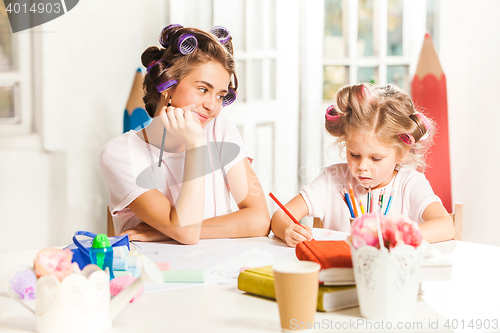 Image of The young mother and her little daughter drawing with pencils at home