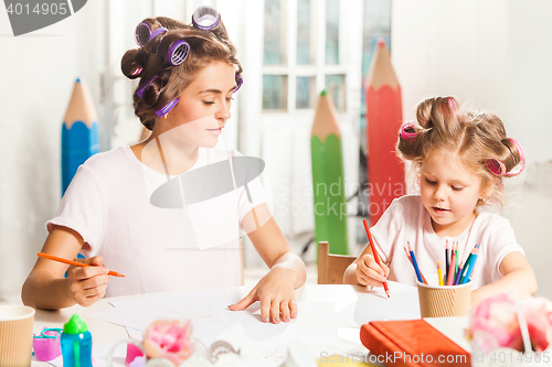 Image of The young mother and her little daughter drawing with pencils at home