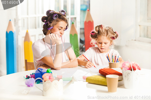 Image of The young mother and her little daughter drawing with pencils at home