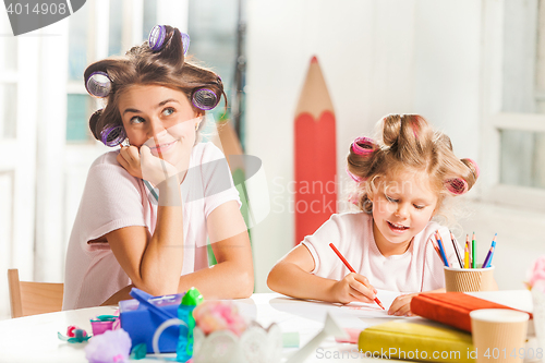 Image of The young mother and her little daughter drawing with pencils at home