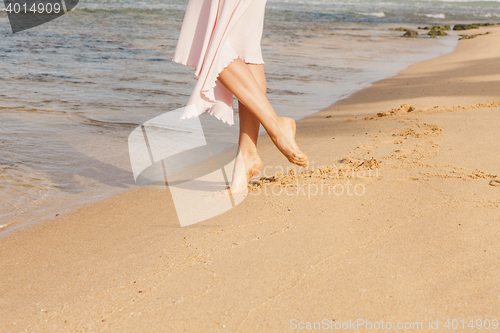 Image of Woman legs walking on the beach sand