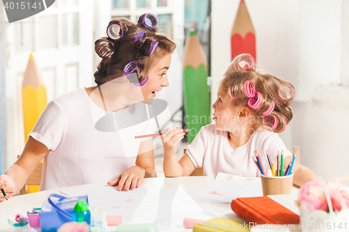 Image of The young mother and her little daughter drawing with pencils at home