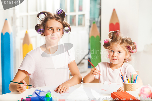 Image of The young mother and her little daughter drawing with pencils at home