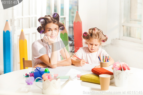 Image of The young mother and her little daughter drawing with pencils at home