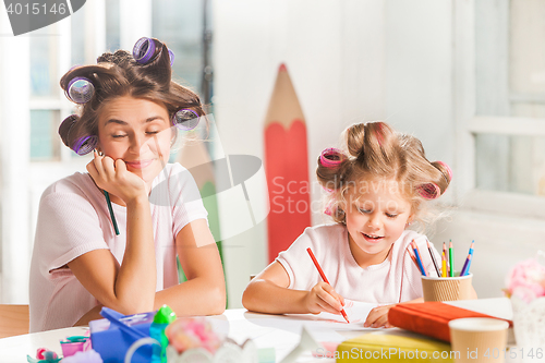 Image of The young mother and her little daughter drawing with pencils at home