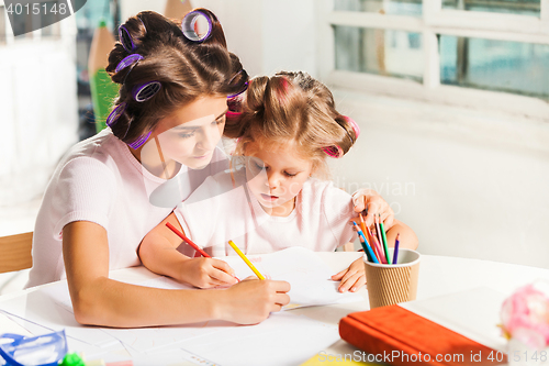 Image of The young mother and her little daughter drawing with pencils at home