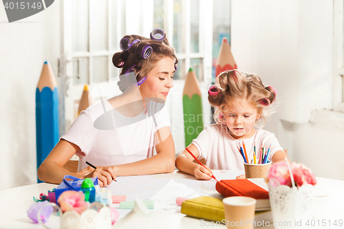 Image of The young mother and her little daughter drawing with pencils at home