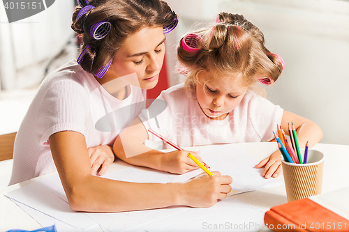 Image of The young mother and her little daughter drawing with pencils at home