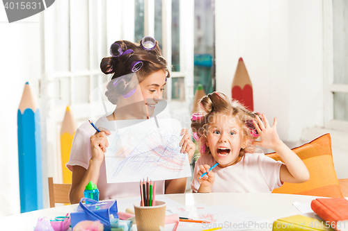 Image of The young mother and her little daughter drawing with pencils at home