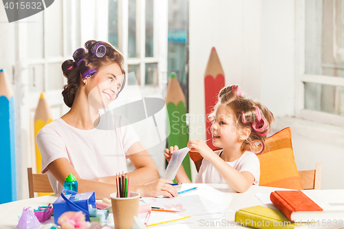 Image of The young mother and her little daughter drawing with pencils at home