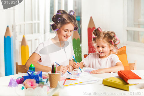 Image of The young mother and her little daughter drawing with pencils at home