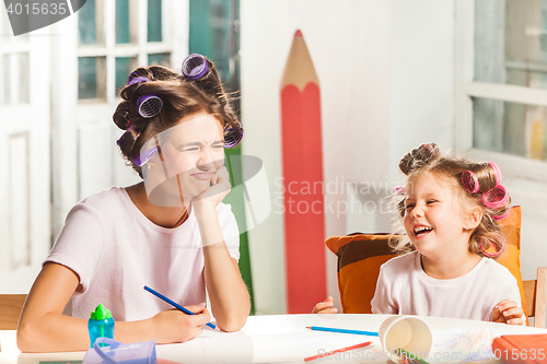 Image of The young mother and her little daughter drawing with pencils at home