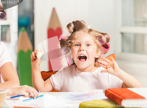 Image of The young mother and her little daughter drawing with pencils at home