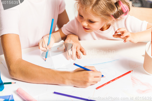 Image of The young mother and her little daughter drawing with pencils at home