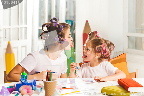 Image of The young mother and her little daughter drawing with pencils at home