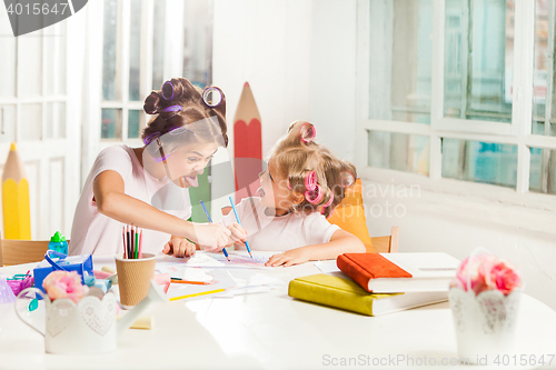 Image of The young mother and her little daughter drawing with pencils at home